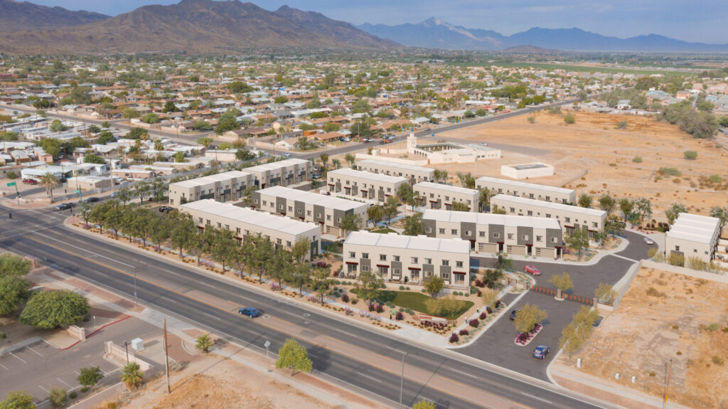 Aerial view of a housing complex with multiple buildings, surrounded by roads and sparse vegetation, set against a backdrop of mountains and a sprawling suburban area, showcasing the meticulous plumbing in the new construction.